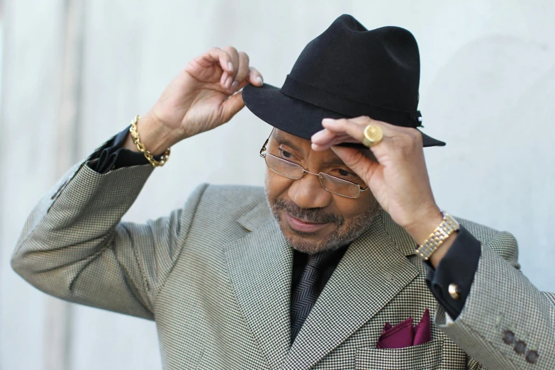 a man in a suit and hat adjusts his hat, inspired by George Barret, Sr., unsplash, george clinton, wearing a suit and glasses, holding it out to the camera, rodney matthew