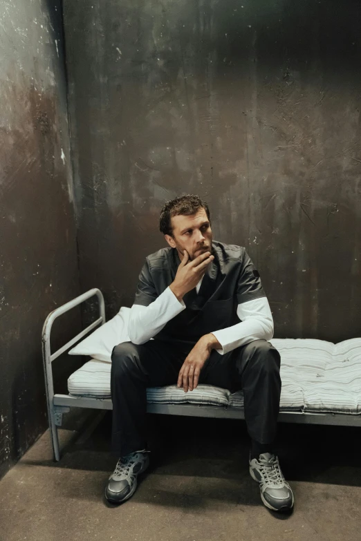 a man sitting on a bed in a room, an album cover, inspired by Tibor Czorba, unsplash, in a prison cell, taking a smoke break, handsome man, artem