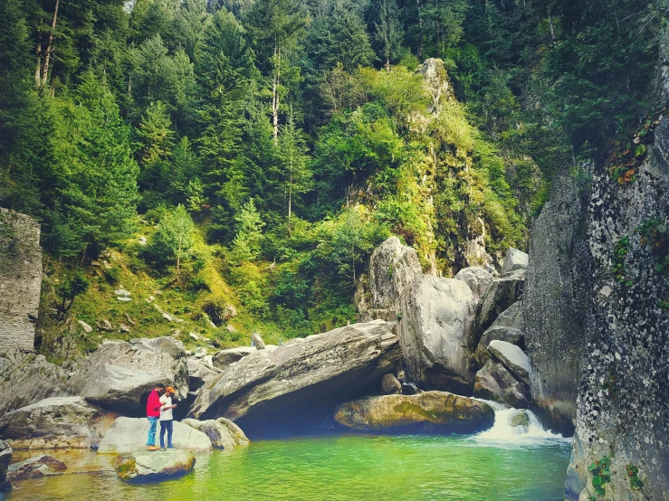 a couple of people standing on a rock next to a river, by Muggur, in green forest, instagram photo, pools of water, uttarakhand