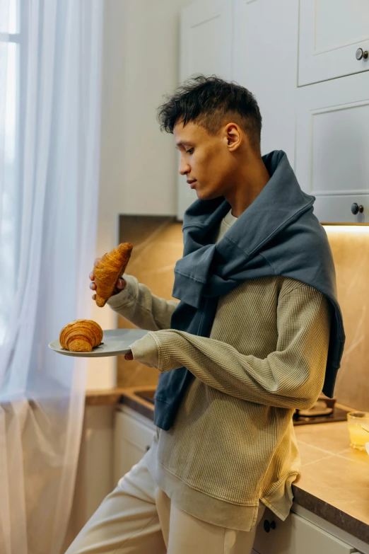 a man standing in a kitchen holding a plate of food, cozy aesthetic, profile image, bread, man wearing a closed cowl