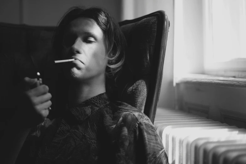 a man sitting in a chair with a cigarette in his mouth, a black and white photo, inspired by Lasar Segall, unsplash, orelsan, delicate androgynous prince, inspired in balthus, relaxing after a hard day