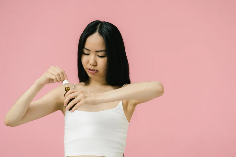 a woman in a white tank top holding a bottle of perfume, trending on pexels, process art, acupuncture treatment, young asian girl, elongated arms, pink halter top