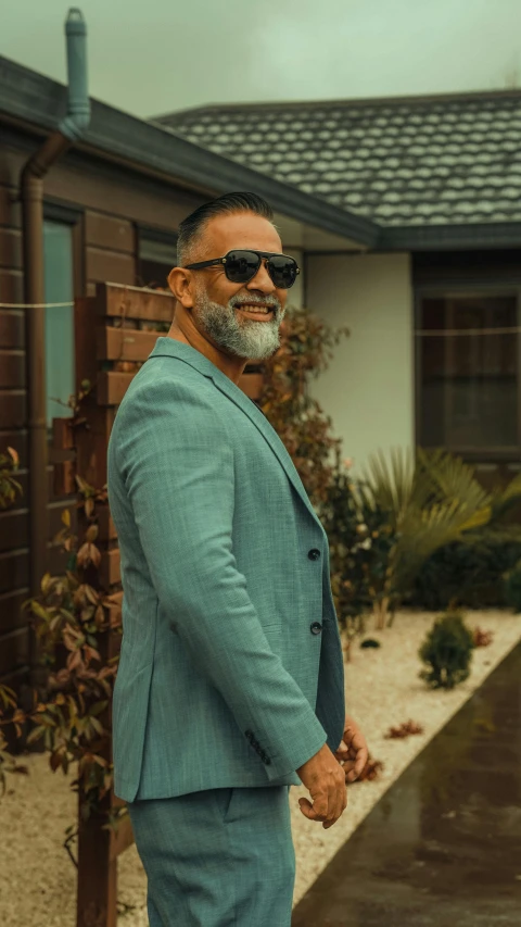 a man in a suit and sunglasses standing in front of a house, pexels contest winner, temuera morrison, grey trimmed beard, full body image, profile image
