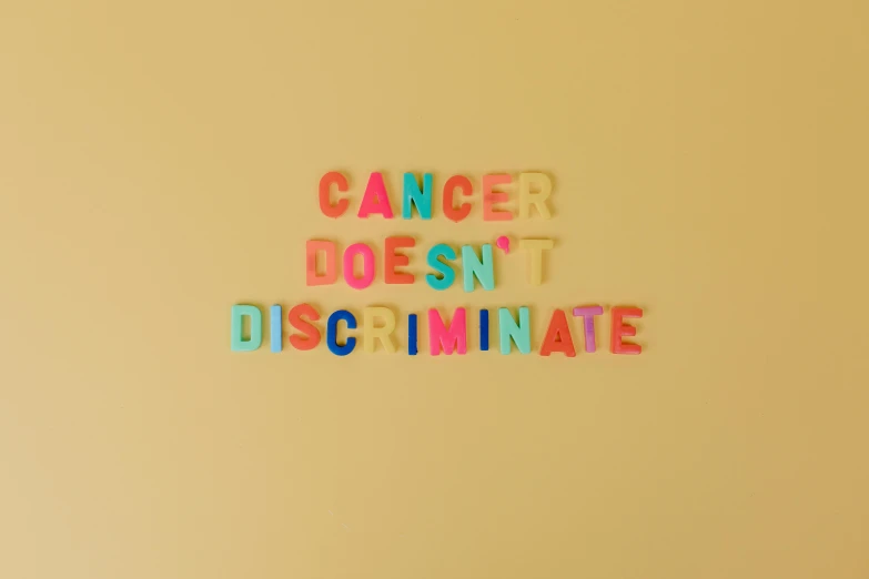 a sign that says cancer doesn't discriminate, by Caro Niederer, pexels, feminist art, colors: yellow, multi - coloured, 5, healthcare