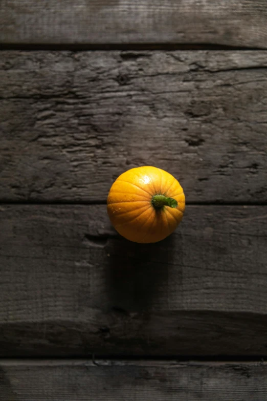 an orange sitting on top of a wooden table, in front of a black background, mustard, with slight stubble, pumpkin