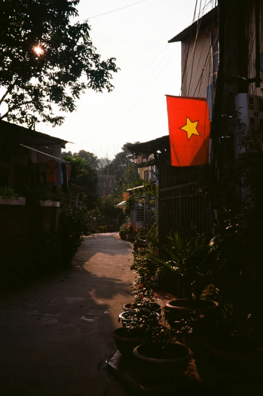 a vietnamese flag hanging from the side of a building, an album cover, unsplash, in a village street, color film still, city morning, pathway