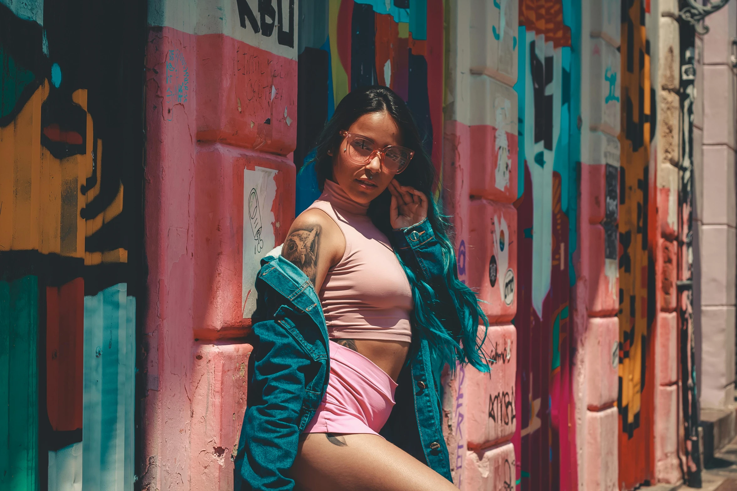 a woman leaning against a wall with graffiti on it, inspired by Elsa Bleda, pexels contest winner, pink body harness, bra and shorts streetwear, shades of pink and blue, beautiful mexican woman