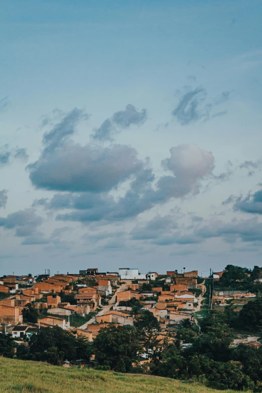 a man flying a kite on top of a lush green hillside, by Elsa Bleda, trending on unsplash, realistic photo of a town, round clouds, brazil, panoramic