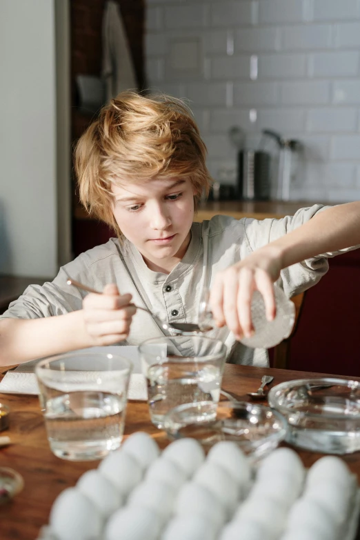 a little boy that is sitting at a table, experimenting in her science lab, red haired teen boy, glass tableware, translucent eggs