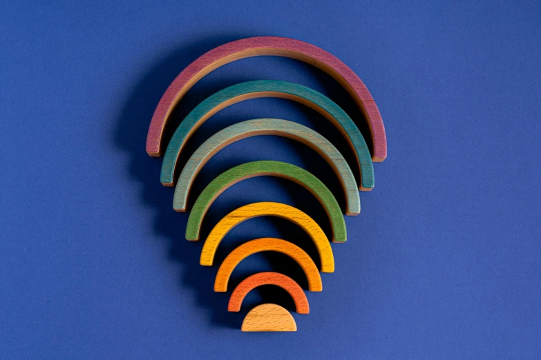 a close up of a wooden object on a blue surface, inspired by Stanton Macdonald-Wright, unsplash, op art, 9 peacock tails, rainbow tubing, different sizes, miniature product photo