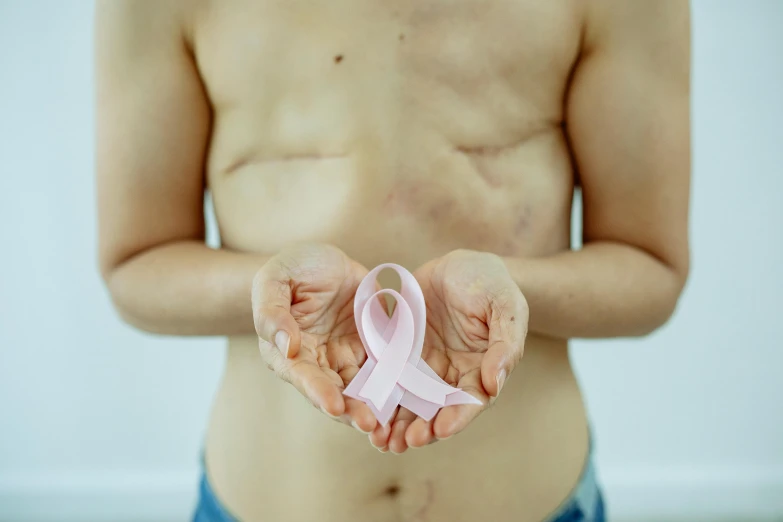 a person holding a pink ribbon in their hands, an album cover, trending on pexels, plasticien, muscle body with battle scars, medical image, bare chest, shaven