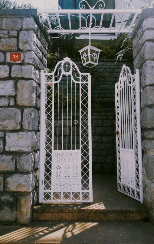 a white iron gate in front of a stone wall, inspired by Edmund Leighton, doors, early 2 0 th century, grotto, 2000