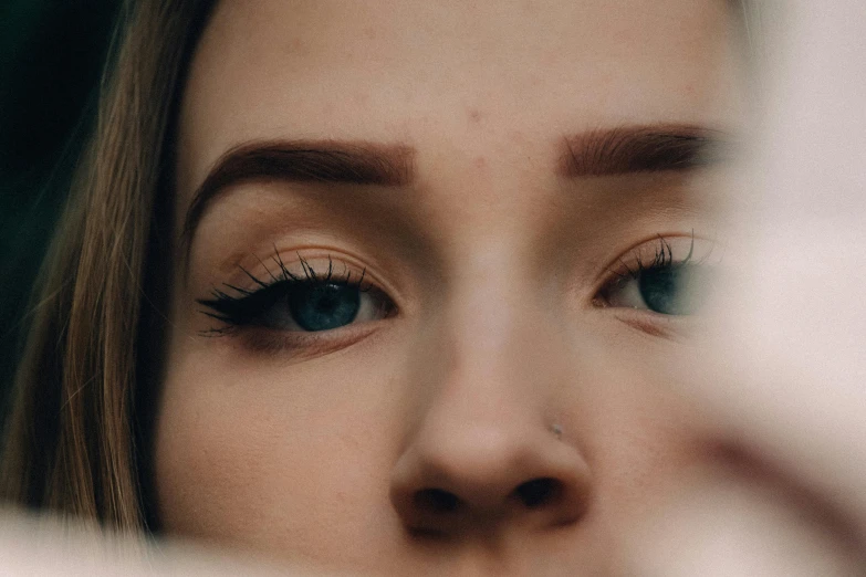 a woman looking at her reflection in a mirror, trending on pexels, hyperrealism, detailed eyes with pupils, teal eyebrows, face closeup, eyebrow scar