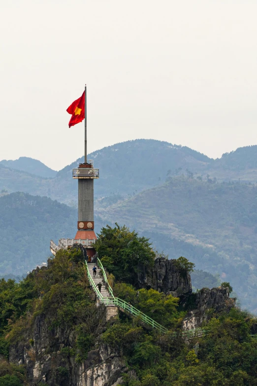 a flag on top of a mountain with mountains in the background, vietnamese temple scene, tower, battlements, monument