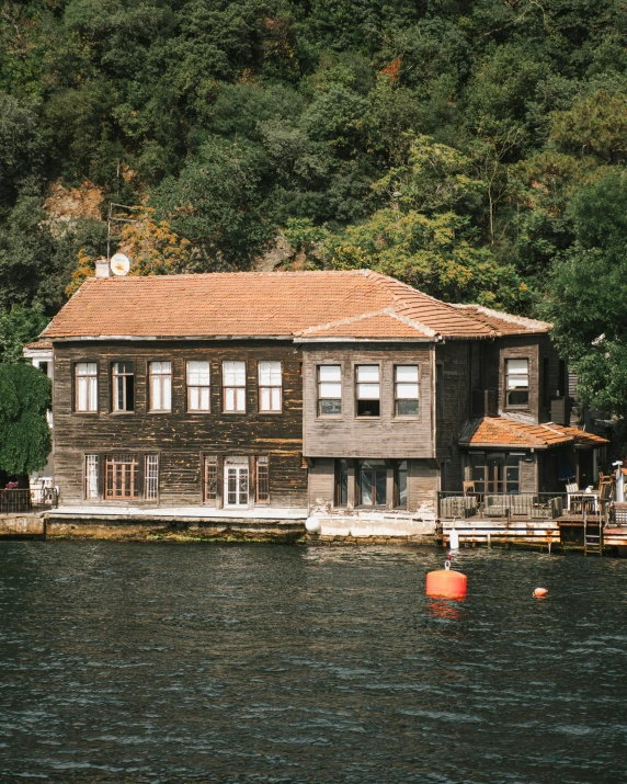 a house sitting on top of a lake next to a forest, by Fikret Muallâ Saygı, pexels contest winner, art nouveau, istanbul, front side, brown, small port village