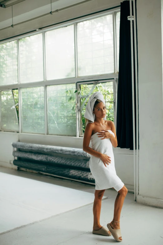 a woman standing in a room with a towel on her head, unsplash, happening, white skirt and barechest, pregnant, morning hour, stretch