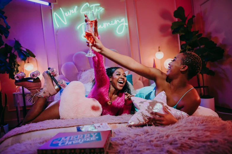 a couple of women sitting on top of a bed, an album cover, trending on pexels, happening, colorful neon signs, drinking champagne, excited, netflix
