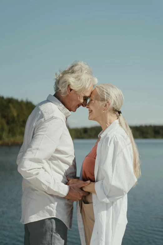 a man and woman standing next to each other near a body of water, by Jaakko Mattila, silver haired, kissing each other, **cinematic, scandinavian