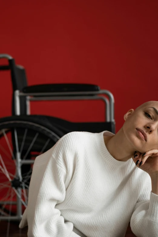 a woman sitting on the floor next to a wheelchair, a portrait, trending on pexels, antipodeans, partially bald, fatigue, non binary model, 15081959 21121991 01012000 4k