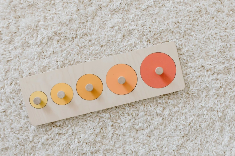 a close up of a toy on a carpet, a jigsaw puzzle, inspired by Alexander Stirling Calder, trending on pexels, bauhaus, orange pastel colors, light circles, in a row, on a wooden plate