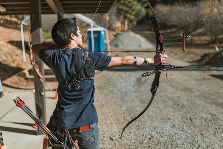 a man that is standing in the dirt with a bow, profile image, action sports, front facing shot, indoor shot