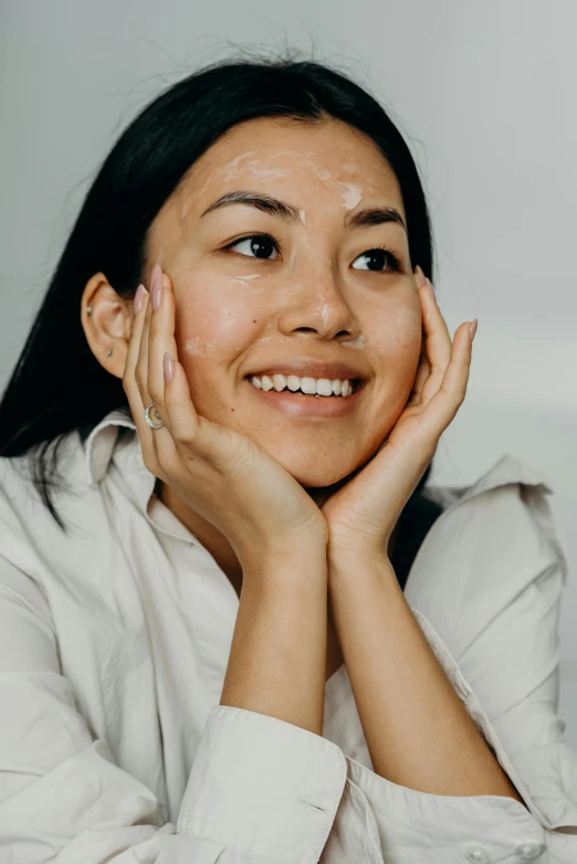 a woman sitting at a table with her hands on her face, inspired by Ruth Jên, trending on pexels, smiling mask, korean face features, silicone skin, frontal picture