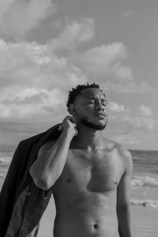 a man standing on top of a beach next to the ocean, a black and white photo, inspired by Xanthus Russell Smith, : kendrick lamar, posing on the beach, bare chest, brown skin