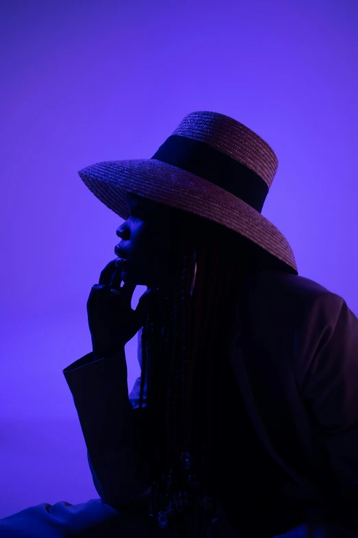 a woman in a hat talking on a cell phone, an album cover, pexels contest winner, afrofuturism, dramatic lowkey studio lighting, blue and purle lighting, adut akech, with backlight