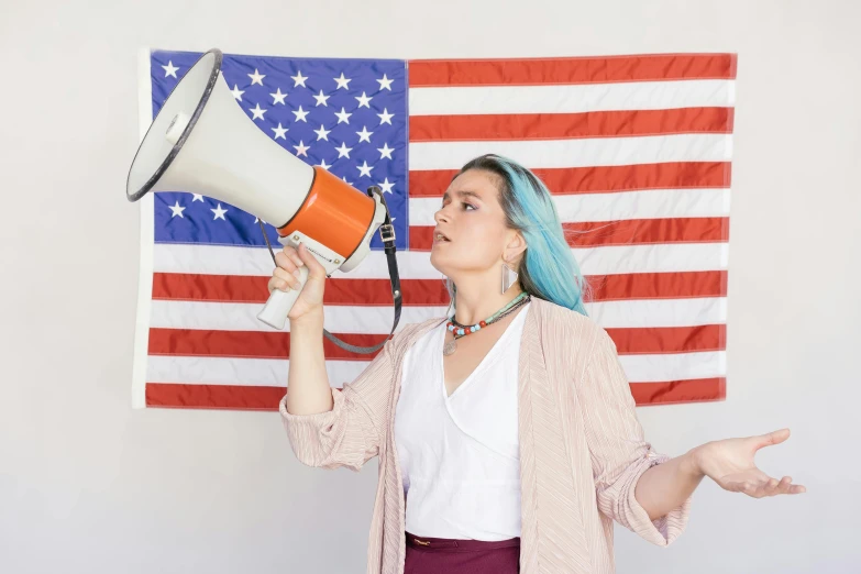 a woman holding a megaphone in front of an american flag, pexels, american realism, non binary model, 🚿🗝📝, profile image, background image