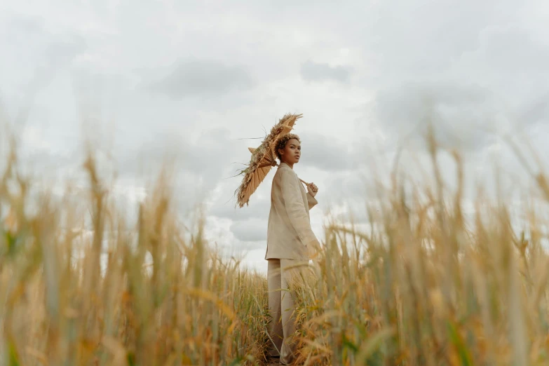 a woman standing in a field of tall grass, by Emma Andijewska, pexels contest winner, straw hat and overcoat, afrocentric mysticism, girl walking in wheat field, cardboard