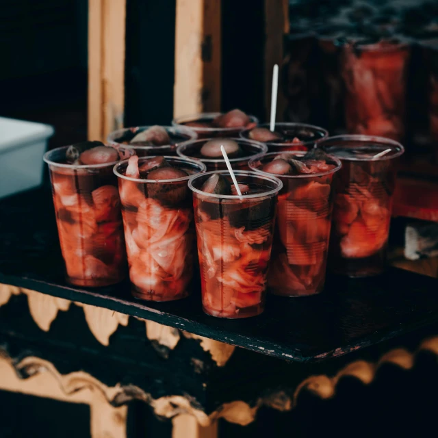 a table topped with plastic cups filled with fruit, by Adam Marczyński, pexels, trapped in tall iced tea glass, dark red and black color palette, round thighs, punk party