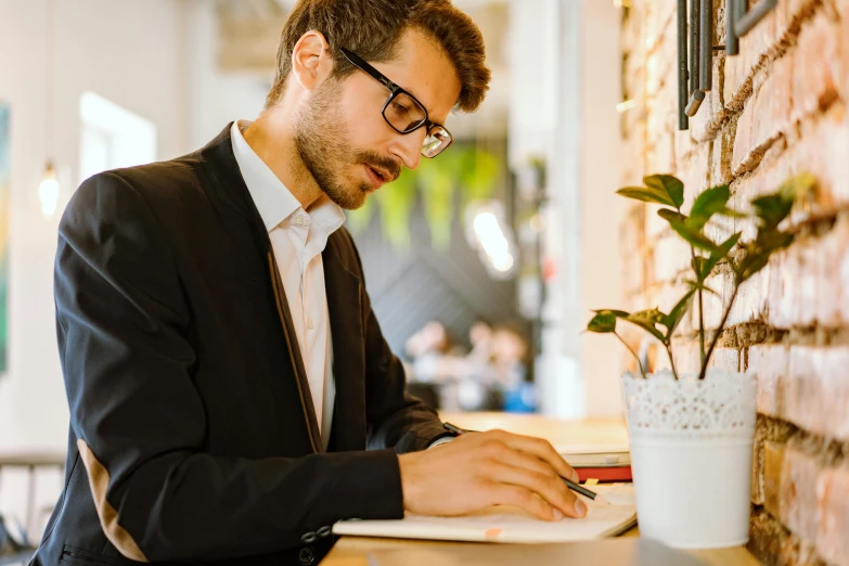 a man sitting at a table working on a laptop, by Julia Pishtar, pexels contest winner, academic art, wearing a suit and glasses, lachlan bailey, a handsome, raphael lecoste