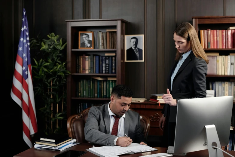 a man and a woman sitting at a desk in front of a computer, lawyer suit, te pae, on a dark background, working in an office