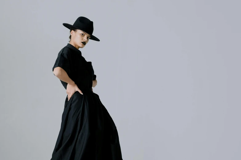 a woman in a black dress and hat, inspired by Josefina Tanganelli Plana, unsplash, bauhaus, in front of white back drop, wide skirts, androgyny, style of yoshii chie