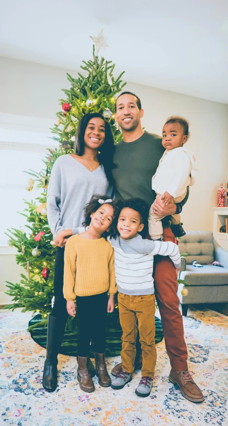 a family poses in front of a christmas tree, a portrait, by Carey Morris, pexels, incoherents, an olive skinned, john krasinski, square, african american