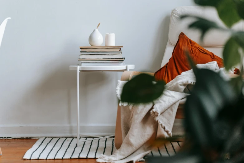 a white chair sitting on top of a hard wood floor, by Emma Andijewska, pexels contest winner, stack of books on side table, orange and white color scheme, someone sits in bed, white candles