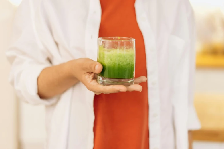 a woman holding a glass of green liquid, unsplash, moringa juice, multiple stories, green and white, standing sideways