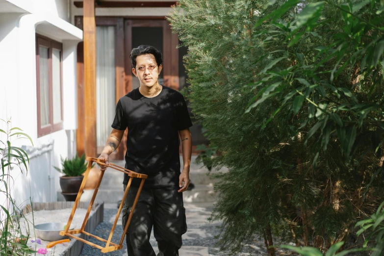 a man walking down a sidewalk carrying a chair, a portrait, by Basuki Abdullah, with matsu pine trees, vanta black, in front of the house, avatar image