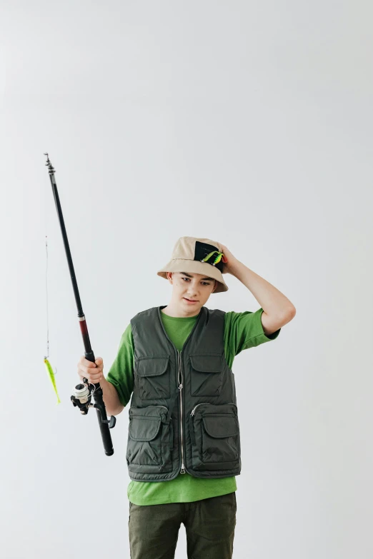 a boy in a green shirt is holding a fishing rod, trending on pexels, tall hat, model is wearing techtical vest, plain background, lachlan bailey