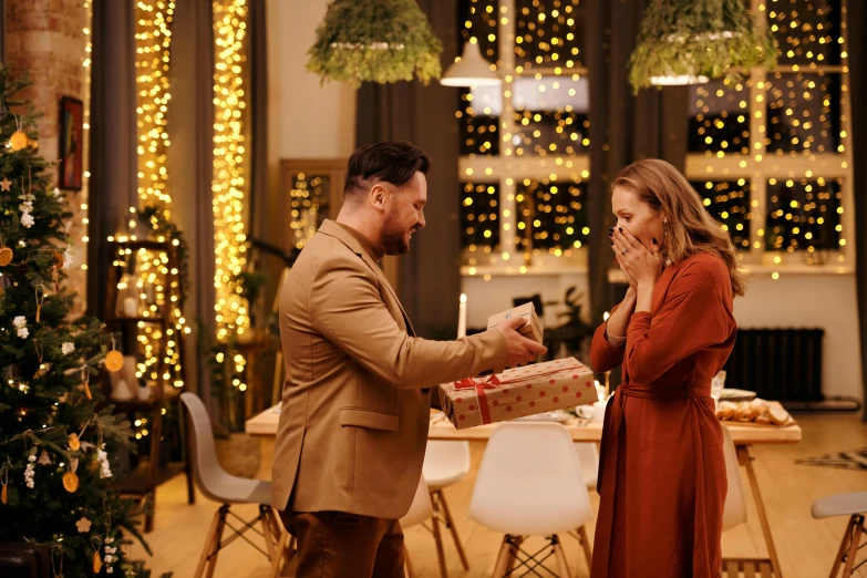 a man giving a woman a present in front of a christmas tree, pexels contest winner, hurufiyya, scene from a dinner party, brown, actor, 😭🤮 💔