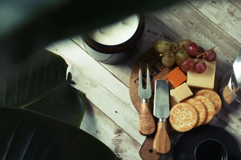 a wooden cutting board topped with cheese and crackers, a still life, unsplash, cutlery, summer lighting, dark. no text, natural candle lighting