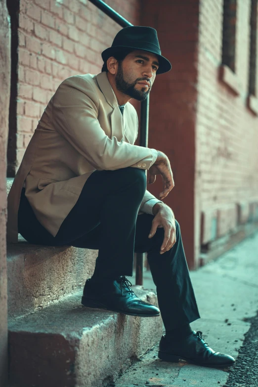 a man sitting on the steps of a building, by Andrew Stevovich, pexels contest winner, black stetson and coat, tan suit, thinking pose, very attractive man with beard