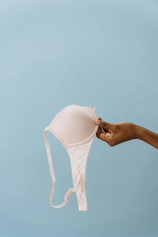 a woman's hand holding a bra in front of a blue background, unsplash, light pink, back arched, milk, facing front