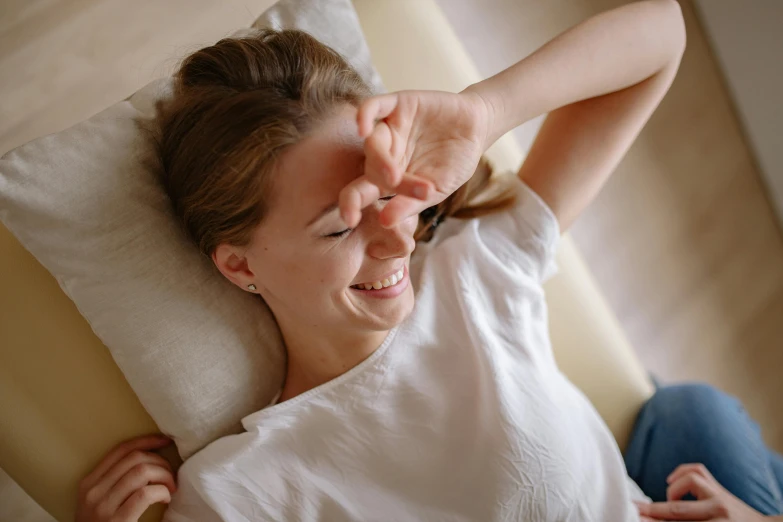 a woman laying on top of a bed next to a pillow, pexels contest winner, happening, hands shielding face, mischievous grin, acupuncture treatment, relaxing on the couch