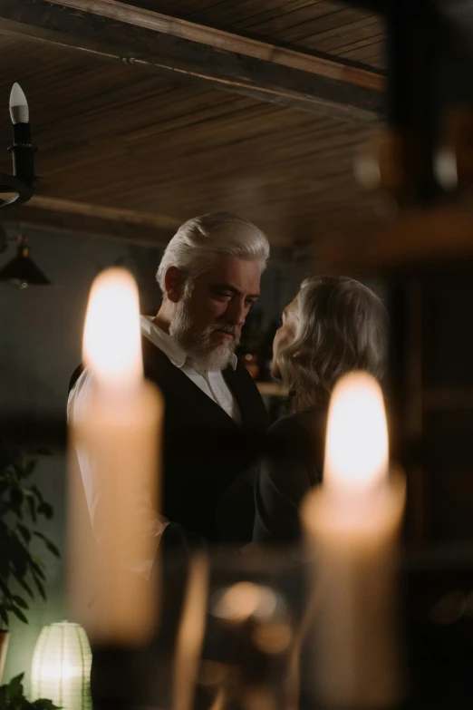 a man and a woman standing next to each other, by Dan Frazier, pexels contest winner, romanticism, white candles, white hair and white beard, cinematic still frame, a seance