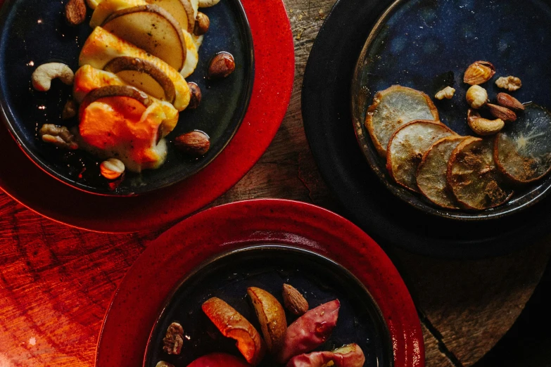 three plates of food sitting on top of a wooden table, by Julia Pishtar, cheese and salami on the table, raku, in a red dish, thumbnail