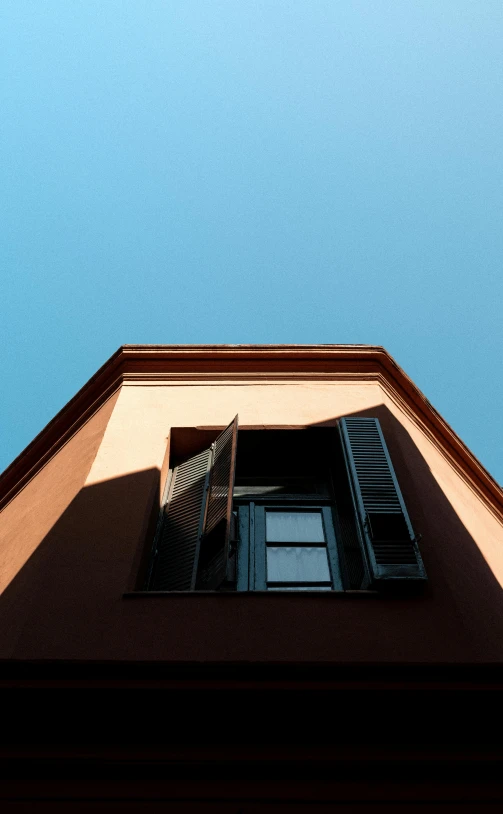 a tall building with a blue sky in the background, inspired by Ricardo Bofill, pexels contest winner, postminimalism, sunny bay window, burnt sienna and venetian red, worm\'s eye view, gambrel roof