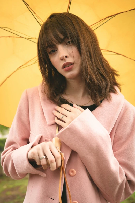 a woman in a pink coat holding a yellow umbrella, inspired by Elsa Bleda, trending on pexels, photorealism, brown hair and bangs, rings, sydney sweeney, natural soft pale skin