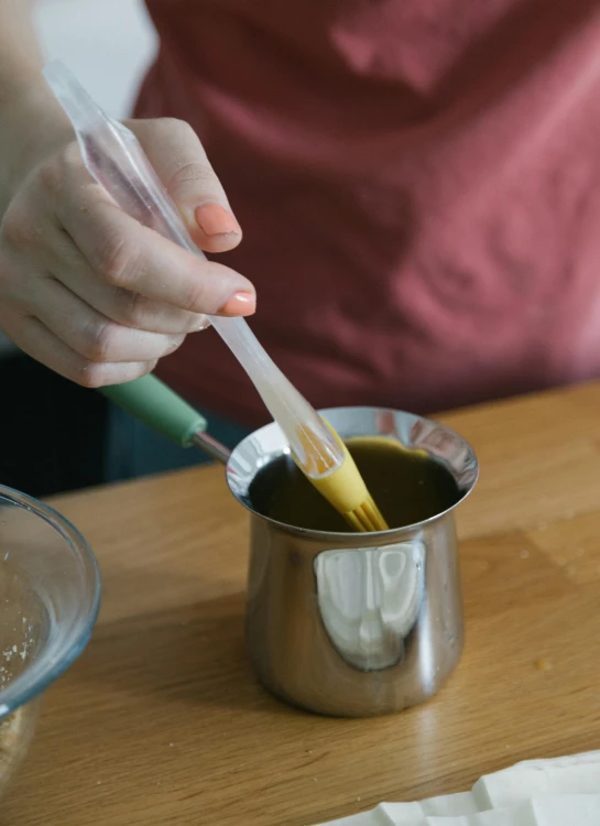 a person stirring something in a cup on a table, dripping oil, detailed product image, tall shot, mustard