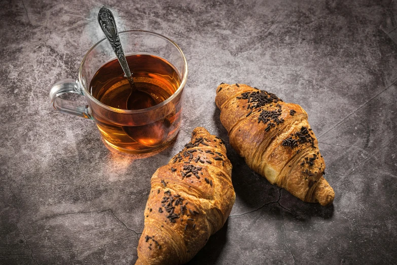 two croissants next to a cup of tea, trending on pexels, hyperrealism, on a gray background, dark and dim, high quality product image”, professionally post-processed